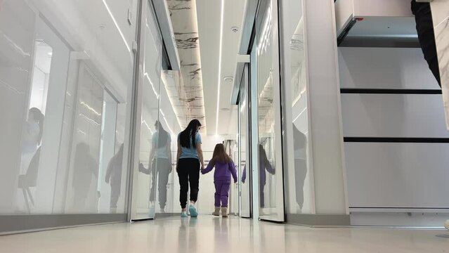woman and girl walk along corridor look at each other large white hall transparent glass white doors reflection hospital hospital care concept help children dentistry children's hospital go