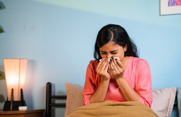 Young girl suffering from cold by sneezing at home whille sleeping on bed - concept of healthcare,...