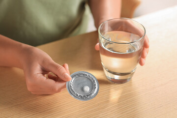 Woman taking emergency contraception pill at wooden table indoors, closeup