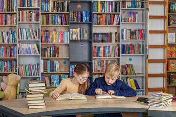 Little school children reading books together while sitting at table in library. Back to school