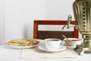 Vintage samovar, cup of hot drink and snacks served on white wooden table. Traditional Russian tea ceremony
