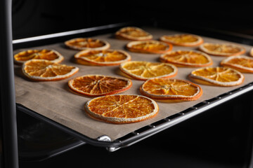 Many dry orange slices on parchment paper in oven