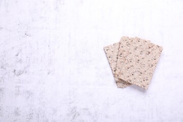Tasty crispbreads on white textured table, top view. Space for text