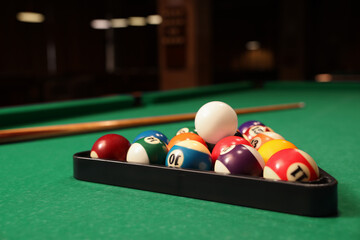 Plastic triangle rack with billiard balls and cue on green table indoors, space for text - obrazy, fototapety, plakaty