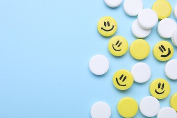 Many antidepressant pills with happy faces on light blue background, flat lay. Space for text
