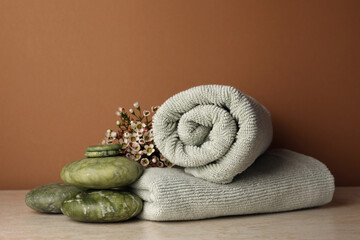 Composition with spa stones, towels and flowers on beige table against brown background. Space for text