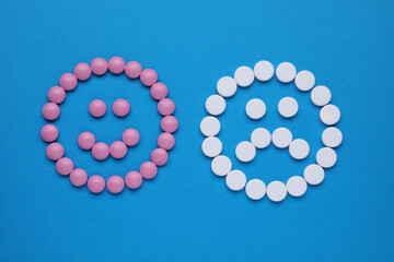 Sad and happy emoticons made of antidepressants on blue background, flat lay