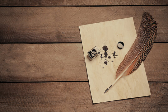 Feather pen, inkwell and vintage parchment with ink stains on wooden table, top view. Space for text
