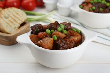Delicious beef stew with carrots, peas and potatoes on white wooden table, closeup