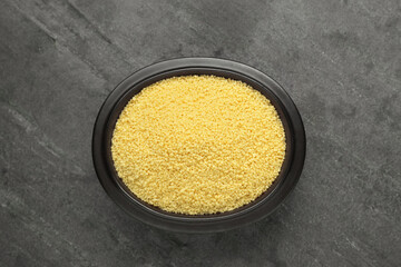 Bowl of raw couscous on grey table, top view