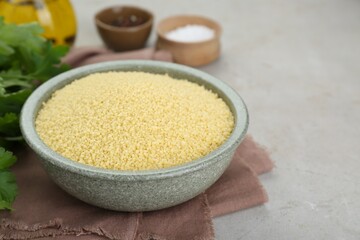 Bowl of raw couscous on light table, closeup. Space for text
