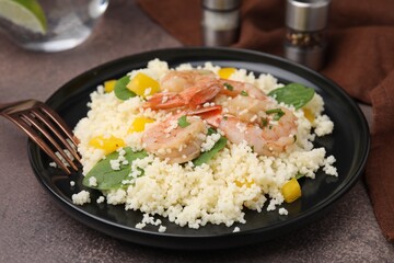 Tasty couscous with shrimps, bell pepper and basil on brown textured table, closeup