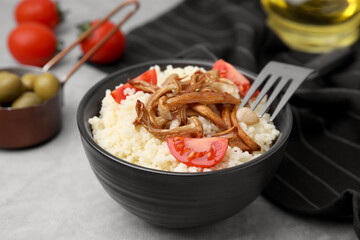 Tasty couscous with mushrooms and tomatoes on grey table, closeup