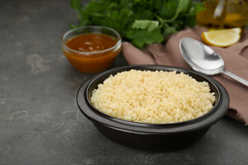 Bowl of tasty couscous on grey table, space for text