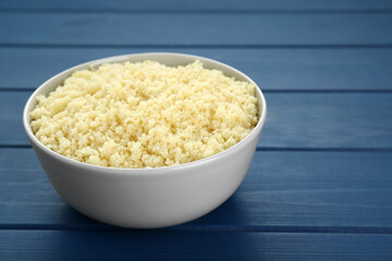 Bowl of tasty couscous on blue wooden table, closeup. Space for text
