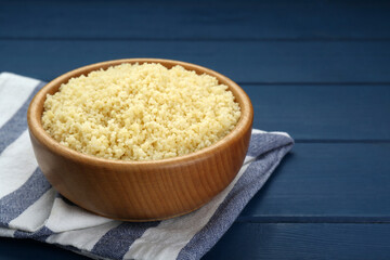 Bowl of tasty couscous on blue wooden table, closeup. Space for text