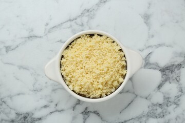 Bowl of tasty couscous on white marble table, top view