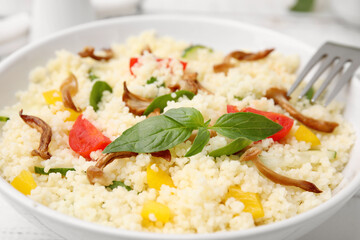 Bowl of delicious couscous with vegetables and basil, closeup