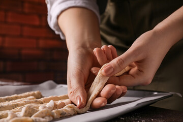 Woman putting homemade breadsticks on baking sheet at wooden table indoors, closeup. Cooking traditional grissini