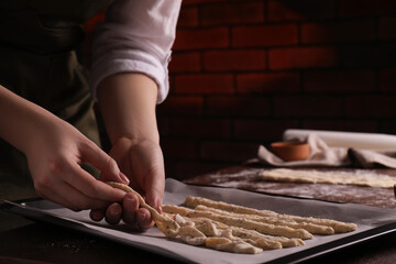 Woman putting homemade breadsticks on baking sheet at wooden table indoors, closeup. Cooking traditional grissini