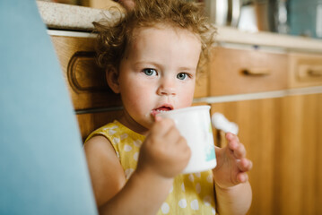 Child girl is drinking water in the kitchen at home.