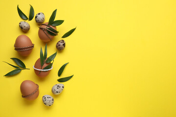 Easter eggs decorated with green leaves on yellow background, flat lay. Space for text