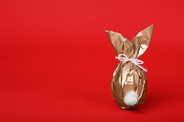 Easter bunny made of shiny gold paper and egg on red background. Space for text