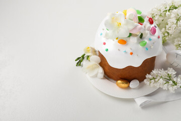 Traditional Easter cake with sprinkles, jelly beans, marshmallows and decorated eggs on white table, space for text