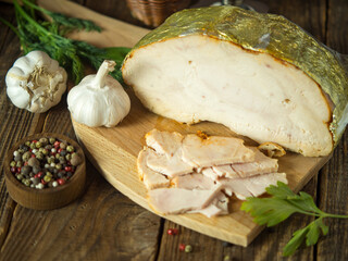 homemade boiled pork whole and sliced, smoked lies on a wooden cutting vintage board on a rustic background.boiled pork