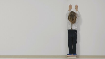 Little kid stand on books stack with hands up trying to reach the top