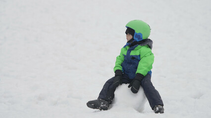 Fototapeta na wymiar Little child with ski equipment sit on snow ball waiting for winter sport