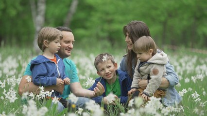 Naklejka na ściany i meble Parents and three children portrait in blossom daffodils field