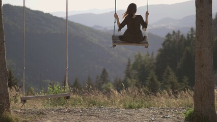 Young woman feels like flying over the mountains in a rope wooden swing