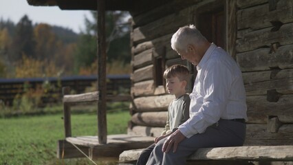 Grandson enjoy talking with grandfather on wooden porch of rustic house