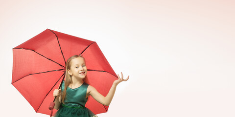 Portrait of a happy smiling child girl in green dress holding ambrella on pink background with space for text.