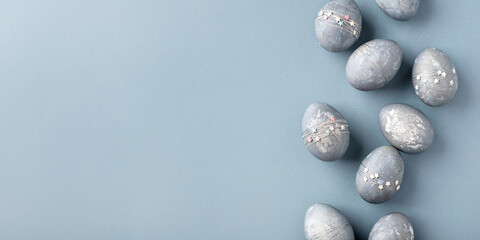 Festive Easter background. Gray-blue Easter eggs with stars on a blue table. Banner with a place for text. Top view.