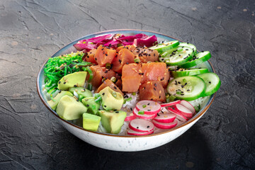 Tuna poke bowl with avocado, cucumbers, wakame, radish, and purple cabbage, a healthy Hawaiian dish with rice, on a black background