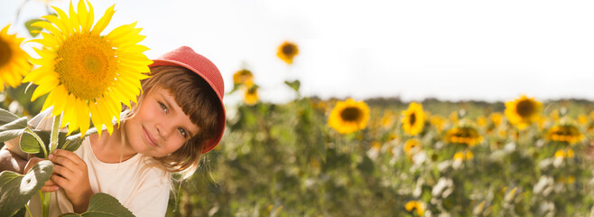 funny little child girl wearing a straw hat with a sunflower in a field with sunflowers. Slow life. Enjoying the little things. banner