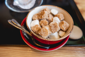 Red bowl with two types of sugar - white and cane sugar. Sweet cubes for hot beverage in cafe.