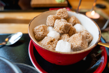 Red bowl with two types of sugar - white and cane sugar. Sweet cubes for hot beverage in cafe.
