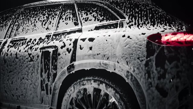 Aesthetic Slow Motion Footage of a Black Family SUV Covered in Washing Soap and Foam. Close Up Shot of Foam Dripping from Car's Rear Wheel Arch onto the Electric Car's Tyre and Rim