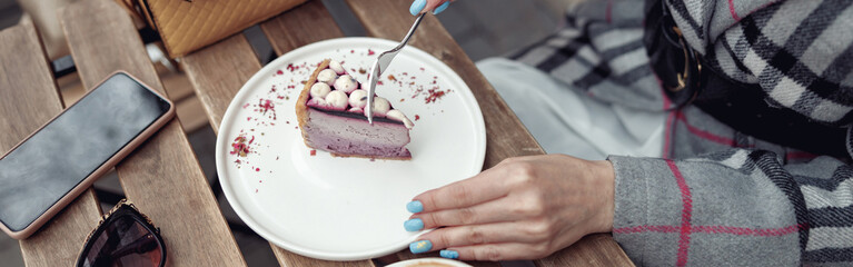 Top view on female with blue manicure eating cheesecake with cappuccino at table outside.