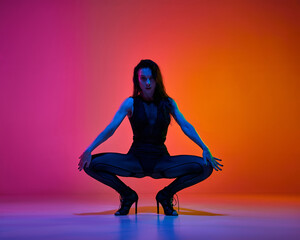 Expressive beautiful young woman in stylish clothes and heeled shoes posing on gradient red pink background in neon light. Dancer. Contemporary dance style, art, aesthetics, hobby, creative lifestyle