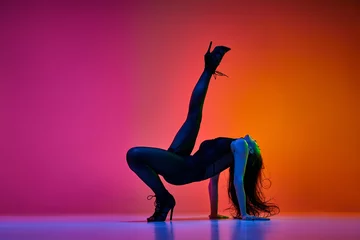 Gordijnen Flexibility. Young woman, professional dancer performing high heel dance over gradient red pink studio background in neon light. Concept of contemporary dance style, art, aesthetics, hobby, creativity © master1305