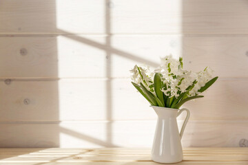 Home interior with Easter decor. Spring flowers in a vase, indoor plant on the background of a wooden white wall