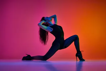 Poster Flexibility and passion. Young woman dancing high heel, contemp dance over gradient pink red studio background in neon light. Contemporary dance style, art, aesthetics, hobby, creative lifestyle © master1305