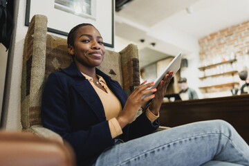Young african woman sitting in arm-chair and using digital tablet