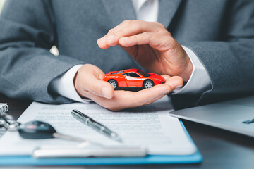 Business woman's hand protecting red toy car on desk. Planning to manage transportation finance...