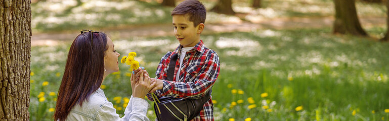 Pretty mother smelling flowers from small son in park. Woman with dandelions and child.