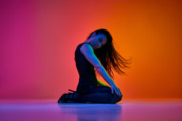 Expressive dance. Young woman, stiletto dancer performing over gradient pink orange studio background in neon light. Concept of contemporary dance style, art, aesthetics, hobby, creative lifestyle